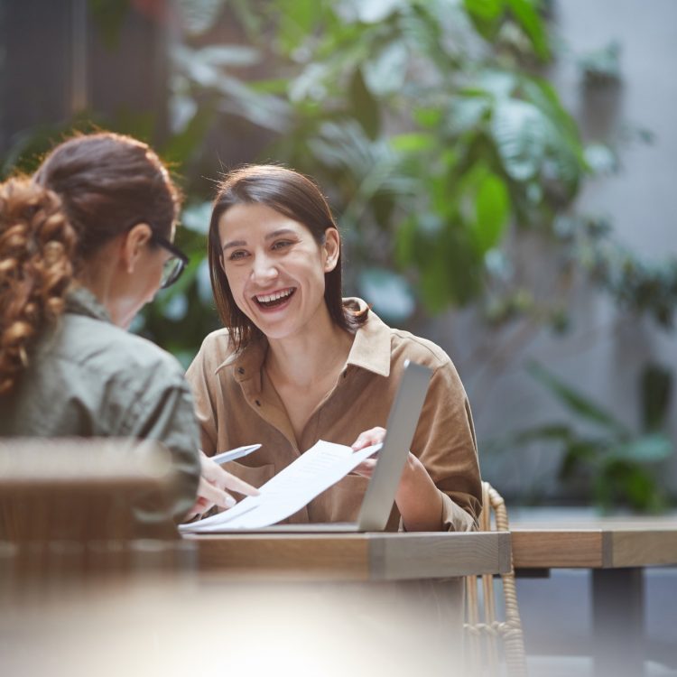Two Smiling Young Women Discussing Business Project in Cafe